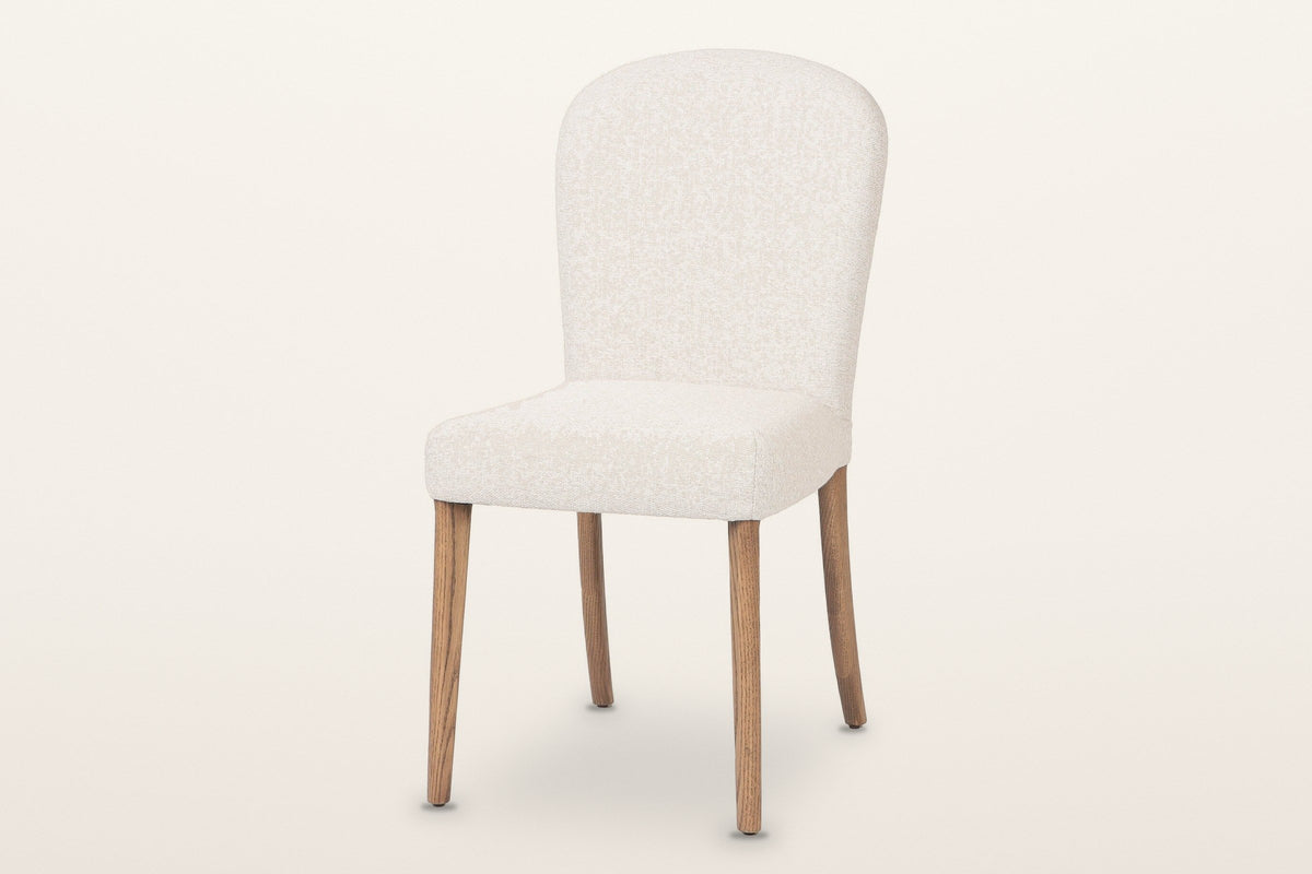 Usseglio dining chair in cream woven fabric on brown ash legs, three-quarter view on a warm white studio backdrop