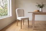 Usseglio dining chair in cream woven fabric beside a bleached-oak table in a Victoria Craftsman dining room, ferns and a Garry oak through the window