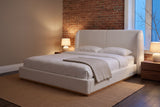 Varenna boucle bed against an exposed brick wall at dusk, two lamps lit on walnut nightstands