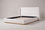 Varenna boucle wingback bed in white, three-quarter view on a warm grey studio backdrop, with its natural wood plinth