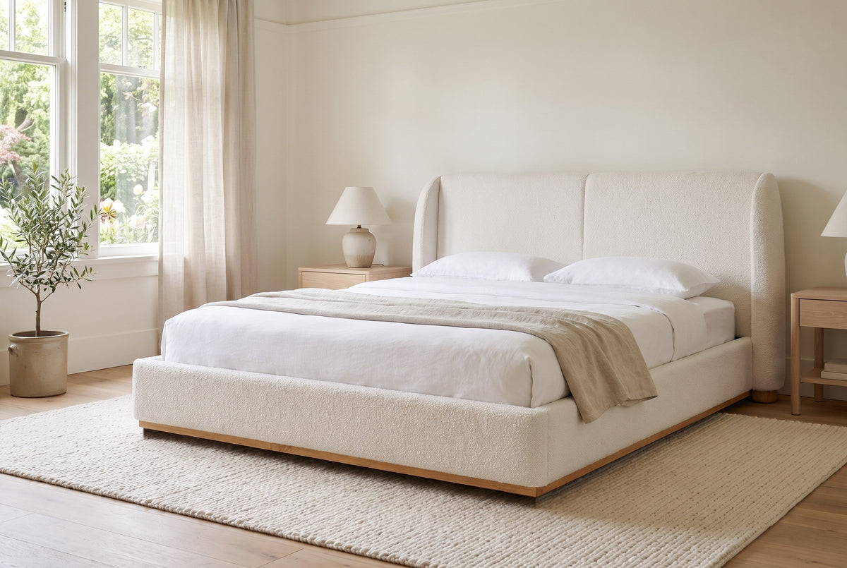 Varenna boucle bed made up with white linen in a bright bedroom with garden windows, linen curtains and an olive tree
