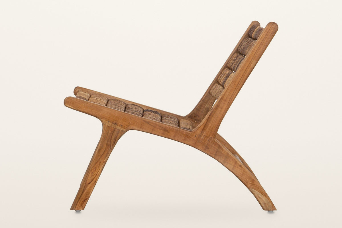 Varigotti accent chair from the side on a warm white studio backdrop: the rail running into one long curved rear leg