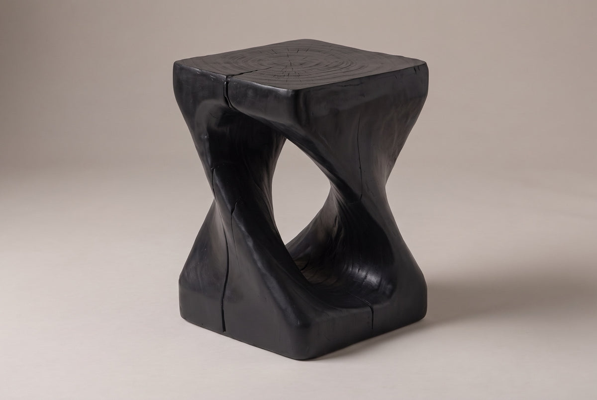 Vicenza twisted side table in Black, seen from the corner on a warm grey studio backdrop: square top, oval opening