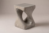 Vicenza twisted side table in Grey, seen from the corner on a warm grey studio backdrop: square top, oval opening
