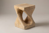 Vicenza twisted side table in Natural, seen from the corner on a warm grey studio backdrop: square top, oval opening