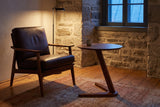 Vigevano side table beside a dark leather armchair in a stone-walled Quebec City sitting room at dusk, a floor lamp lit