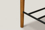 Close-up of a round tapered walnut-finish front leg of the Vigoleno stool with the black metal footrest rods joined into it