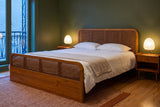 Vinci bed against an olive-green wall at dusk, with two paper lamps lit on wood nightstands and a rust and cream rug
