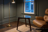 Vipiteno side table beside a tan leather lounge chair in a green-grey Ottawa front room at dusk, a brass floor lamp lit
