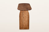 End view of the Visso console table in Pecan on a warm white studio backdrop: the arched face of a solid acacia panel leg und