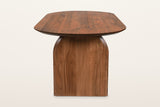 End view of the Visso dining table in Pecan on a warm white studio backdrop: the wide panel leg with arched shoulders under t