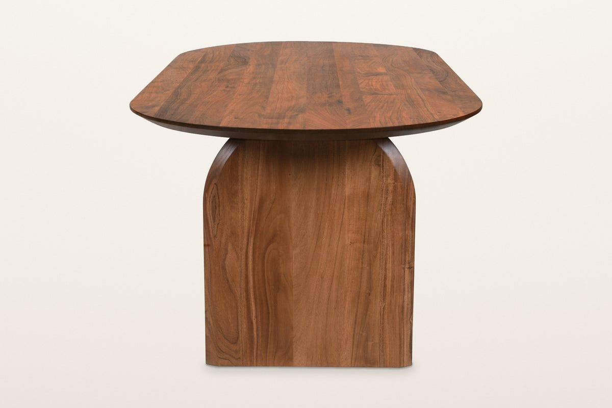 End view of the Visso dining table in Pecan on a warm white studio backdrop: the wide panel leg with arched shoulders under t