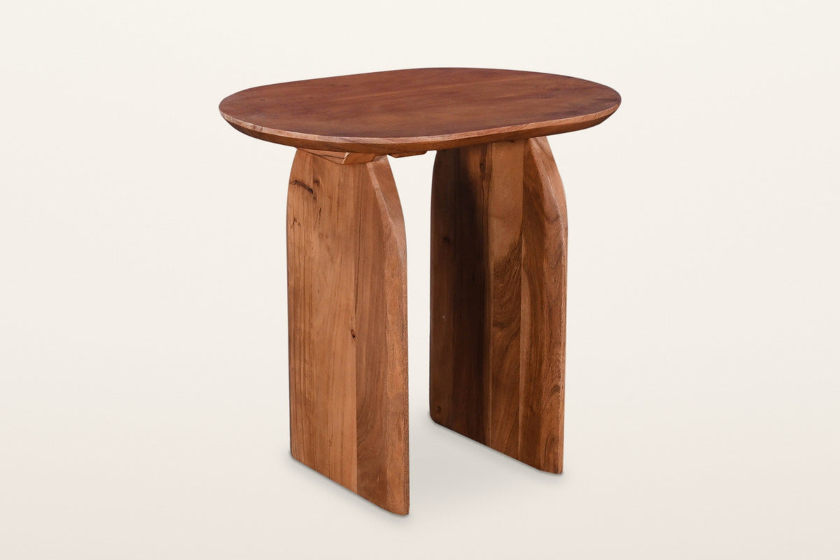 Visso solid acacia side table in Pecan, three-quarter view on a warm white studio backdrop: a soft oval top on two arched pan
