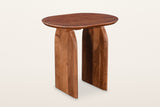 Visso solid acacia side table in Pecan, three-quarter view on a warm white studio backdrop: a soft oval top on two arched pan