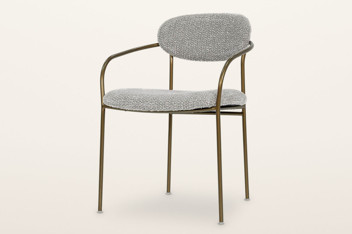 Vitorchiano arm dining chair in Pearl Grey bouclé on a slim antique bronze tube frame, an oval back pad and four straight legs, three-quarter view on a warm white studio backdrop