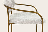 Close-up of the Vitorchiano arm from the side: the antique bronze tube bending from the front leg into the arm and the hoop, above the Pearl Grey bouclé seat
