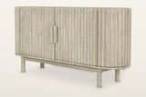 Vitorchiano 63 in sideboard in Natural White Wash acacia: an oval case wrapped in vertical reeds, a split oval wooden pull, four round legs, three-quarter view on a warm white studio backdrop