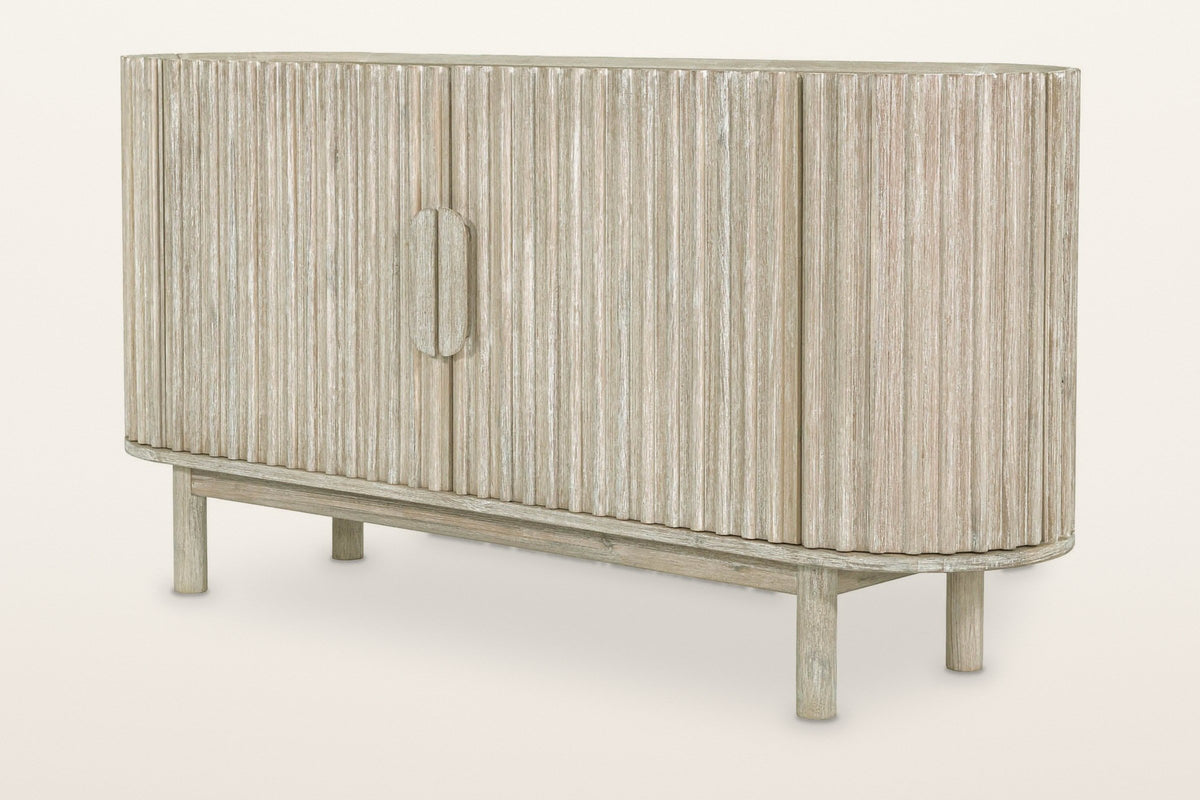 Vitorchiano 63 in sideboard in Natural White Wash acacia: an oval case wrapped in vertical reeds, a split oval wooden pull, four round legs, three-quarter view on a warm white studio backdrop