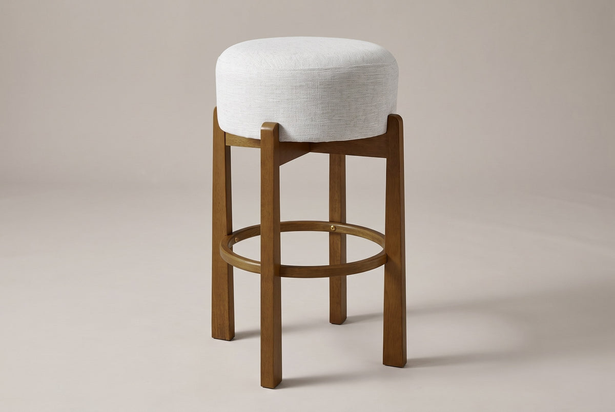 Vogogna backless bar stool in Dark Walnut with an ivory drum cushion, three-quarter view on a warm grey studio backdrop
