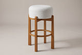 Vogogna backless bar stool in Walnut with an ivory drum cushion, three-quarter view on a warm grey studio backdrop