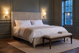 Volterra reeded bed in beige in a panelled bedroom at dusk with brass sconces lit and a linen bench at the foot