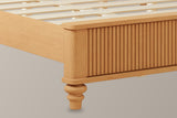 Close-up of the natural-finish reeded footboard corner with its rounded cap and a turned bun foot, the pale slats behind