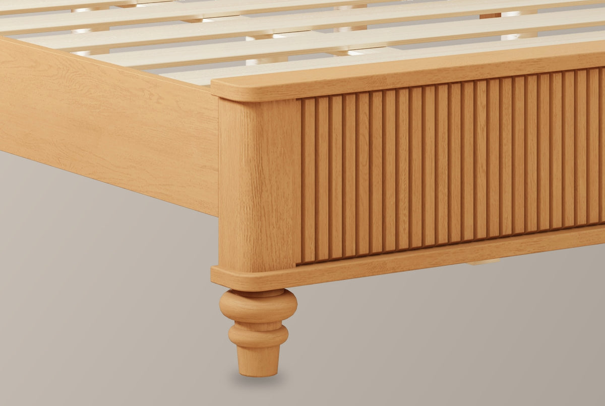 Close-up of the natural-finish reeded footboard corner with its rounded cap and a turned bun foot, the pale slats behind