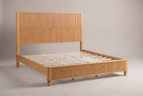 Volterra solid wood reeded bed in a natural honey finish, three-quarter view on a warm off-white studio backdrop