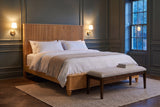 Volterra reeded bed in natural in a panelled bedroom at dusk with brass sconces lit and a linen bench at the foot