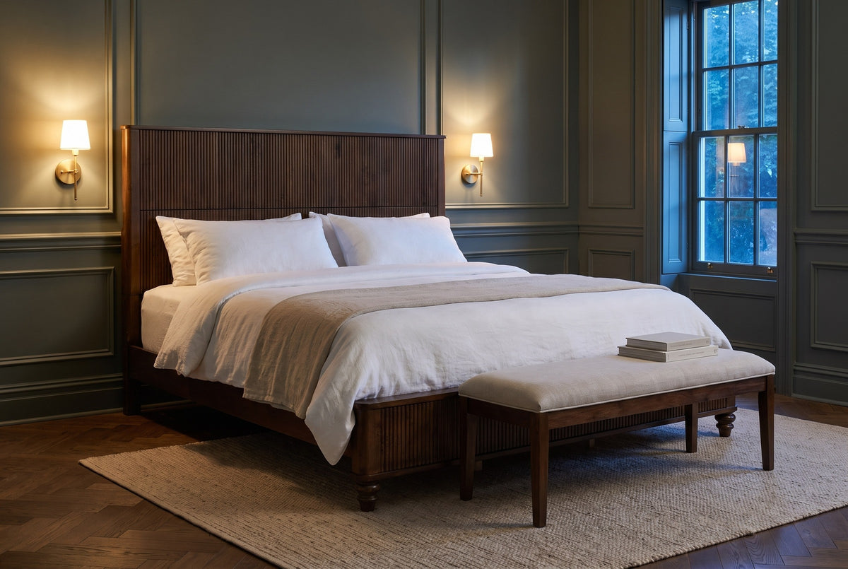 Volterra reeded bed in a panelled bedroom at dusk with brass sconces lit and a linen bench at the foot
