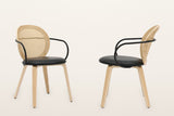 Two of the faux rattan armchairs, front three-quarter and side: the oval cane back in a light oak frame, the black metal arms and the black seat
