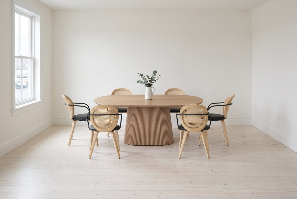 Yale 7-piece dining set in natural oak in a bright Lunenburg dining room: the oval table on its reeded pedestal with six faux rattan armchairs, the harbour through the window