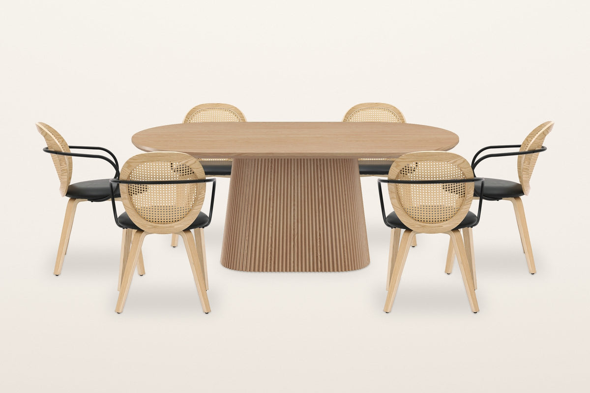 Yale 7-piece dining set in natural oak on a warm white studio backdrop: the oval pedestal table with six cane-back armchairs with black arms and seats