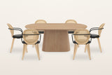 Yale 7-piece dining set in natural oak on a warm white studio backdrop: the oval pedestal table with six cane-back armchairs with black arms and seats